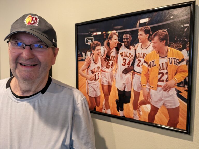 Bob Olson stands in front of a photo of the 1990-91 Northern State men's basketball team he has in his home office.