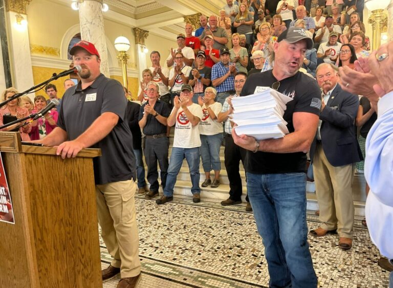 Landowners Mark Lapka of McPherson County, left, and Jared Bossly of Brown County, holding petitions with about 2,000 signatures, speak at the state Capitol in Pierre on July 6, demanding a prohibition against carbon capture pipeline companies gaining access to land against a landowner’s will. South Dakota Searchlight photo by Joshua Haiar