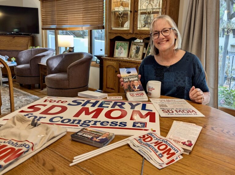 Sheryl Johnson, a Democrat running for U.S. House in South Dakota in 2024, poses with her campaign paraphernalia at her home in Sioux Falls. South Dakota Searchlight photo by Jon Hult.