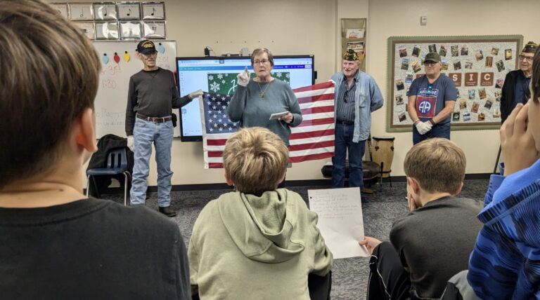 Mike Miller Elementary School students listen while Phyllis Donat, a member of the Veterans of Foreign Wars Post 17 Auxiliary, discusses flag etiquette on Thursday, Nov. 14. Holding the flag are Curtis Bierman, left, and Adam Heyd, members of VFW Post 17. Aberdeen Insider photo by Scott Waltman.