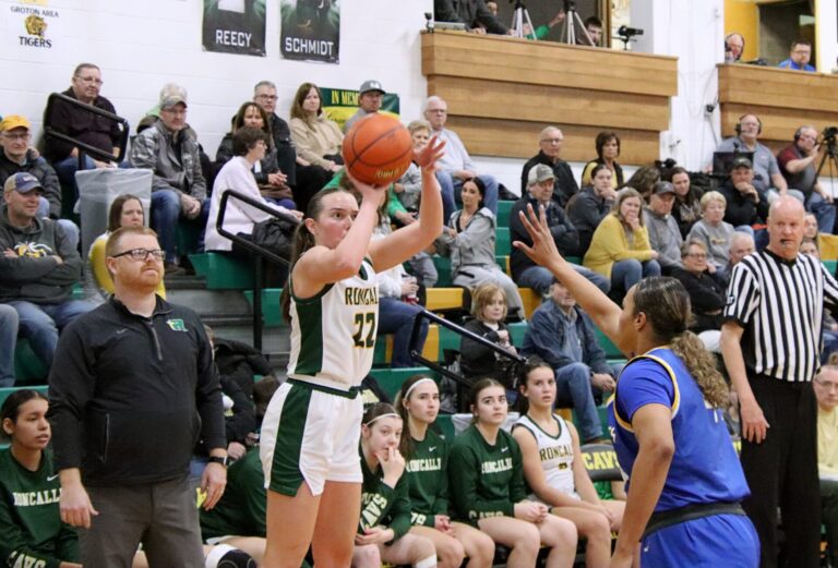 Aberdeen Roncalli's Ava Hanson takes a three-pointer while head coach Derek Larson looks on during a game against Redfield last season. Hanson was an all-state girls basketball player last year as a junior. Aberdeen Insider photo by Robb Garofalo.