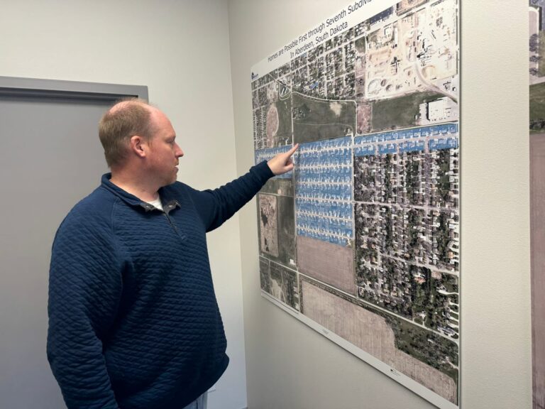 Darin Beckius, executive director of Homes Are Possible Inc., points to maps on the wall in the HAPI offices that show areas of Aberdeen where the nonprofit has developed subdivisions and built new homes. South Dakota News Watch photo by Bart Pfankuch.