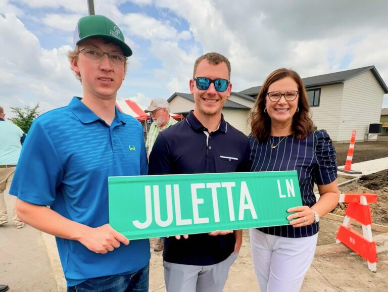 Family members of Juletta Smith, from left, Evan and Brent Dutenhoffer and Catherine Smith, hold the street sign recognizing her work with Homes Are Possible, Inc. Photo courtesy of Homes Are Possible.