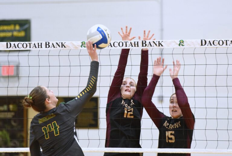 Aberdeen Roncalli's Grace Cogley tips the ball over the block attempt by Milbank's Avery Schuneman (12) and Zora Henrich during their Region 1A match Tuesday, Nov. 4 at the Roncalli Gym. Roncalli advanced in straight sets. Aberdeen Insider photo by Robb Garofalo.