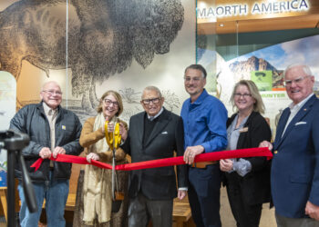 Rosemarie Buntrock cuts a ribbon at the Dacotah Prairie Museum on Tuesday, Dec. 9 as the Rosemarie and Dean L. Buntrock Gallery opens. Also pictured, from left, are Duane Sutton, chairman of the Brown County Commission; Columbia native Dean Buntrock; Aberdeen Mayor Travis Schaunaman; Patricia Kendall, director of the museum; and Terry Birck, project manager for installation of the exhibit. Aberdeen Insider photo by Annie Scott.