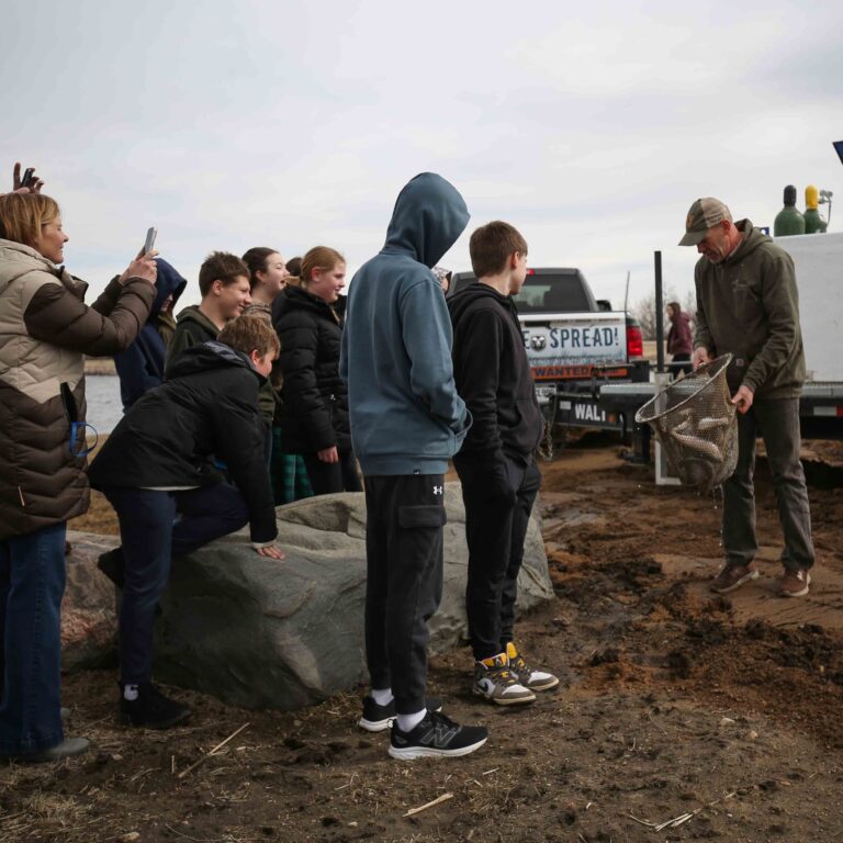 A wildlife officer shows a net full of rainbow trout to a crowd at Pudwill Pond in Leola. The lake was recently stocked to create a fishery. Courtesy photo.