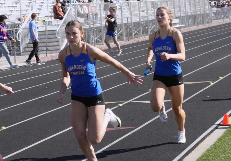 Aberdeen Central's Morgan Griebel reaches back to grab the baton from Mya Arampatzis during the 200-meter relay Friday, April 10 at the Huron Invitational. Photo by Kevin Foss for the Aberdeen Insider.