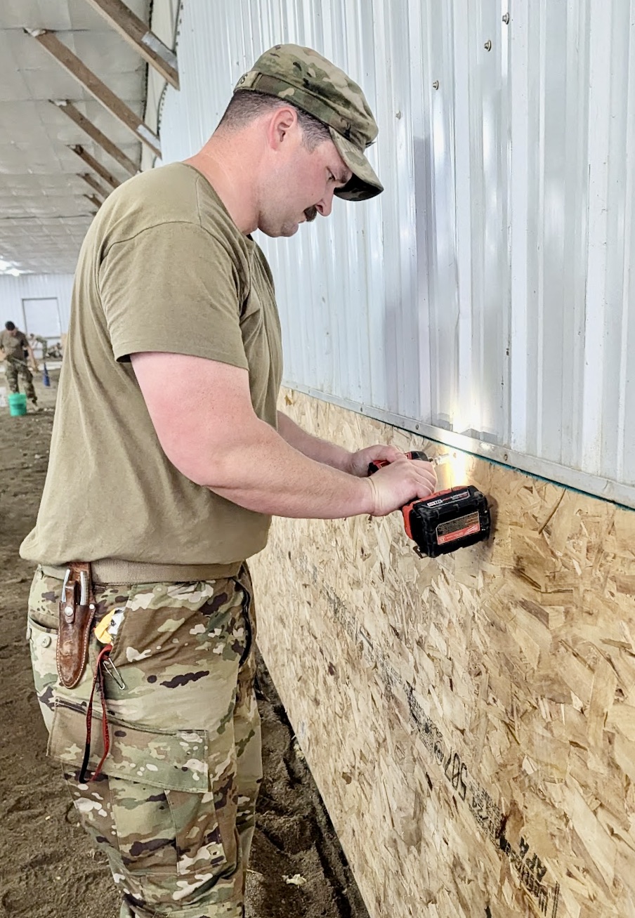 Chris Minkos of Gregory County, a member of the South Dakota National Guard 740th Transportation Co., works to install kickboards on Saturday, June 7 in the arena at SPURS Therapeutic Riding Center. He and other members of the 740th helped with various improvements at SPURS. Aberdeen Insider photo by Scott Waltman.