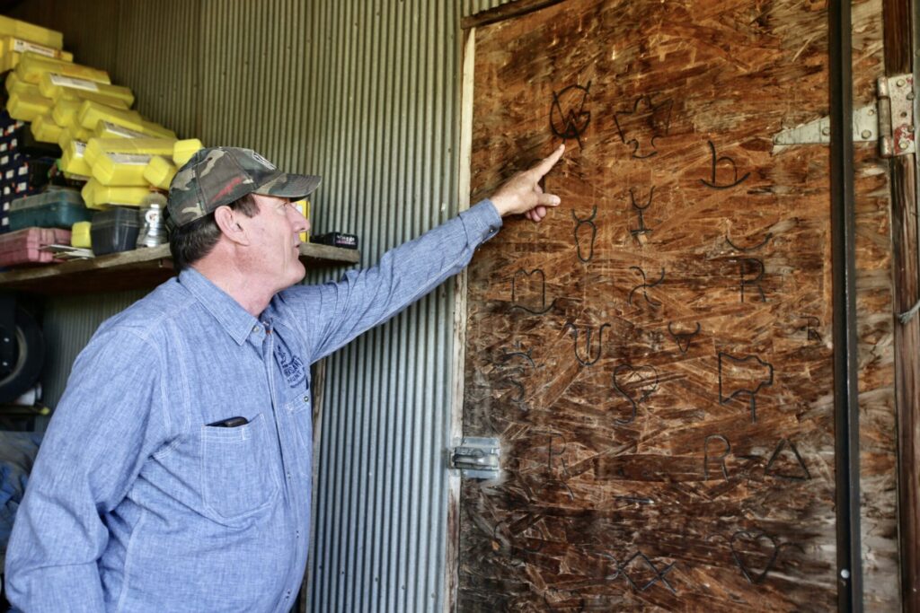 In his welding shop on his ranch in rural Union Center on June 26, South Dakota Gov. Larry Rhoden points to an example of a brand he made into a branding iron. South Dakota Searchlight photo by Photo by Makenzie Huber.